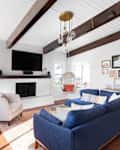 ELMHURST, IL, USA - SEPTEMBER 2, 2020: A renovated modern farmhouse living room with a blue couch, white fireplace, wood beams on a white shiplap ceiling, and a television mounted above the fireplace.