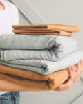 Woman with stack of clean bed sheets on light background