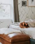 2 people's feet sticking out from under the covers of a bed, sun shining in through window
