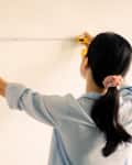 woman measuring wall with measuring tape