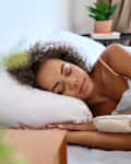 Young calm African American woman model sleeping well on her side with eyes closed lying in comfortable bed on orthopedic mattress lying on soft pillow at home having healthy night sleep relaxing in the morning.