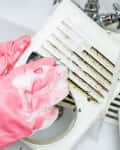 Woman dressed in pink rubber gloves washes with a sponge and soap suds grill of the ventilation return duct blocked by dust and debris.