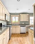 An apartment kitchen with light wood cabinets, stainless steel appliances, and green walls.