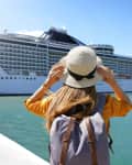 Tourist woman with backpack and hat standing in front of big cruise liner