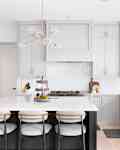 A luxurious kitchen with a large island, gold faucet and sputnik chandelier, stainless steel appliances, and white marble countertops.