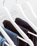 Many blue denim jeans hanging on white clothes hangers on clothing rack. Close up of folded casual denim jeans in wardrobe with coat hangers