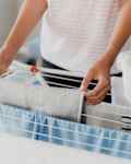 Woman hanging clean wet clothes laundry on drying rack at home laundry room. Detail of female housewife hands closeup holding, spreading and taking laundry basket in front of clothing rack dryer