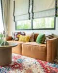 Living room in traditional British cottage furnished with modern looking furniture.  Green and yellow pillows on Leather sofa with green plant pot.