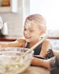 Learning, playing or messy kid baking in kitchen with a young girl smiling with flour on a dirty face at home. Smile, happy or parent cooking or teaching a fun daughter to bake for child development