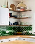 A kitchen detail with butcher block wood countertops, white cabinets, a gold fixture hanging over the island, and green subway tile backsplash.
