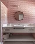 A beautiful modern designed bathroom with cream marble sink, gold wooden framed mirror, matching furniture and walls with decorative pink wallpaper and a shower cubicle with tiled walls