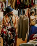 Person browsing racks of clothing in bright thrift store with various garments on display during daylight Peering at different shirts and examining styles and options