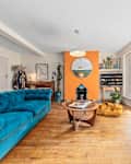 London, UK - April 16th 2025 - Eclectic living room with teal velvet sofa, bold orange fireplace, large windows, and mid-century accents, flooded with natural light.