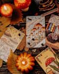 20 July 2025 - Cozy, mystical flat lay of illustrated tarot cards, mushrooms on wooden surface with burning candles, autumn leaves, ferns. Magic, fortune telling, witchcraft
