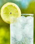 Sparkling water and lemon slice on glass with an ice, sunny day - narrow focus on middle of the glass