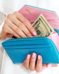 Person placing a five-dollar bill into a blue wallet with a pink interior.