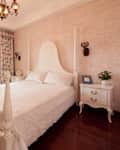 Bright bedroom featuring a white four-poster bed, floral curtains, a potted plant, and a decorative chandelier.