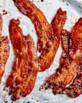 Crispy strips of cooked bacon arranged on parchment paper, showcasing a rich, caramelized color.