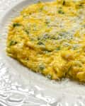 Creamy scrambled eggs with chives, topped with grated cheese, served on a decorative white plate.