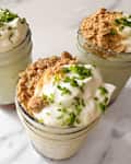 Three jars filled with creamy desserts topped with whipped cream, crushed cookies, and green zest on a marble surface.
