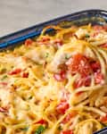 Chicken spaghetti casserole with red bell peppers and melted cheese in a blue dish.