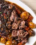 Tender pot roast with carrots, potatoes, and mushrooms in a rich gravy, garnished with fresh herbs.