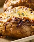 Baked potatoes topped with melted cheese and herbs, oozing on a baking tray.