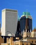 Historic church with brown spires and clock tower, surrounded by modern skyscrapers under a clear blue sky.