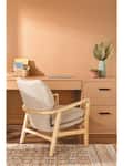 Beige armchair at a wooden desk with a laptop, basket, and decorative vase on a patterned rug.