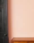 Black door, peach wall, abstract art with dark and light rectangles, and a wooden cabinet.