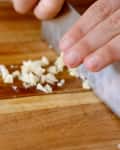 Chopping garlic on a wooden cutting board with a chef's knife.