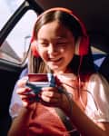 Girl in a car wearing red headphones, playing a handheld game console, smiling.