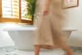 Person walking on a wooden bath mat in a bathroom with a white tub, marble floor, and wooden shutters.