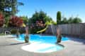 Backyard pool with a yellow slide, surrounded by potted plants and a wooden fence, under a clear blue sky.