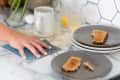 Hand cleaning marble countertop with a blue cloth, next to toast on gray plates, a mug, and glasses of orange juice.