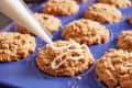 Piping icing onto crumb-topped muffins in a blue Great Jones muffin pan.