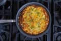 Frittata with green onions in a skillet on a stovetop.