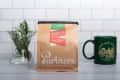 Bag of Partners Coffee Roasters Miracle blend with a green mug and a vase of greenery on a tiled background.