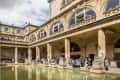 Visitors exploring the Roman Baths, featuring a green pool, classical architecture, and stone columns.