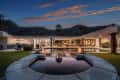 Luxury outdoor patio with pool, fire pit, and mountain view at dusk, surrounded by modern architecture and palm trees.
