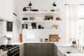 White kitchen with open shelves, gray cabinets, brass faucet, and decor items like cutting boards and vases.