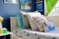 Child's bedroom with blue walls, colorful pillows, wall art, and green curtains.