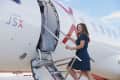 Woman in blue dress boarding a JSX Embraer jet via stairs on a sunny day.