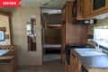 RV interior with wood cabinets, kitchenette, booth seating, and a view into the sleeping area with bunk beds.