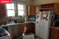 Cluttered kitchen with wooden cabinets, white fridge covered in photos, and granite countertops under a double window.
