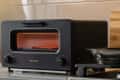 Black Balmuda toaster oven on a kitchen counter with bread inside.
