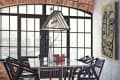 Industrial-style dining room with glass table, black chairs, geometric rug, and large windows.