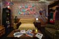 Living room with alphabet wall lights, yellow crocheted sofa, patterned wallpaper, and vintage decor.
