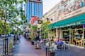 Street view of a coffee house with outdoor seating, people dining, and a tall building in the background.