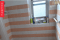 Bathroom with peach and white striped tiles, bathtub, towel, and toiletries on window ledge.